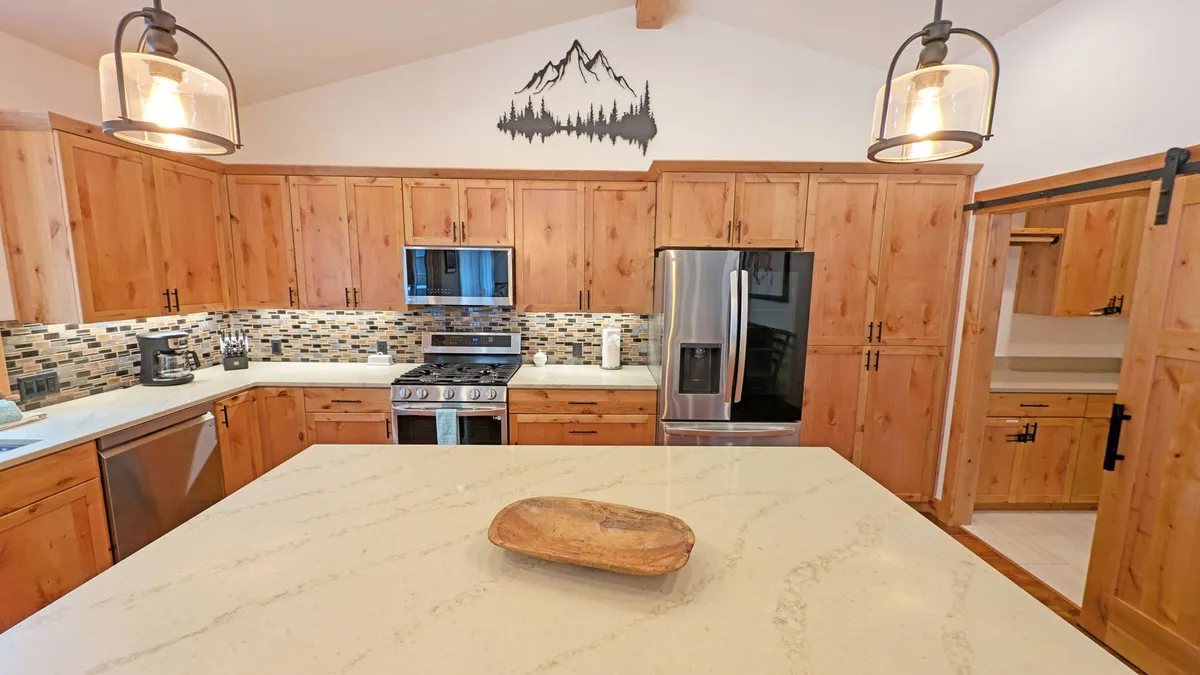 A close-up view of the kitchen highlights the central island, stainless steel gas range, and quality wood cabinetry. The warm tones and thoughtful decor create a welcoming space designed for both casual breakfasts and celebratory dinners.
