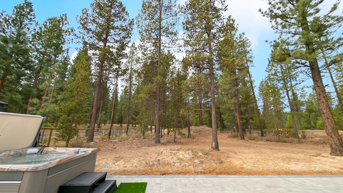 This image centers on the hot tub set amidst tall pines and cleared ground, reinforcing the secluded feel. The hot tub is surrounded by forest, suggesting direct access to trails and wildlife, and the open sky hints at opportunities for stargazing or morning coffee.