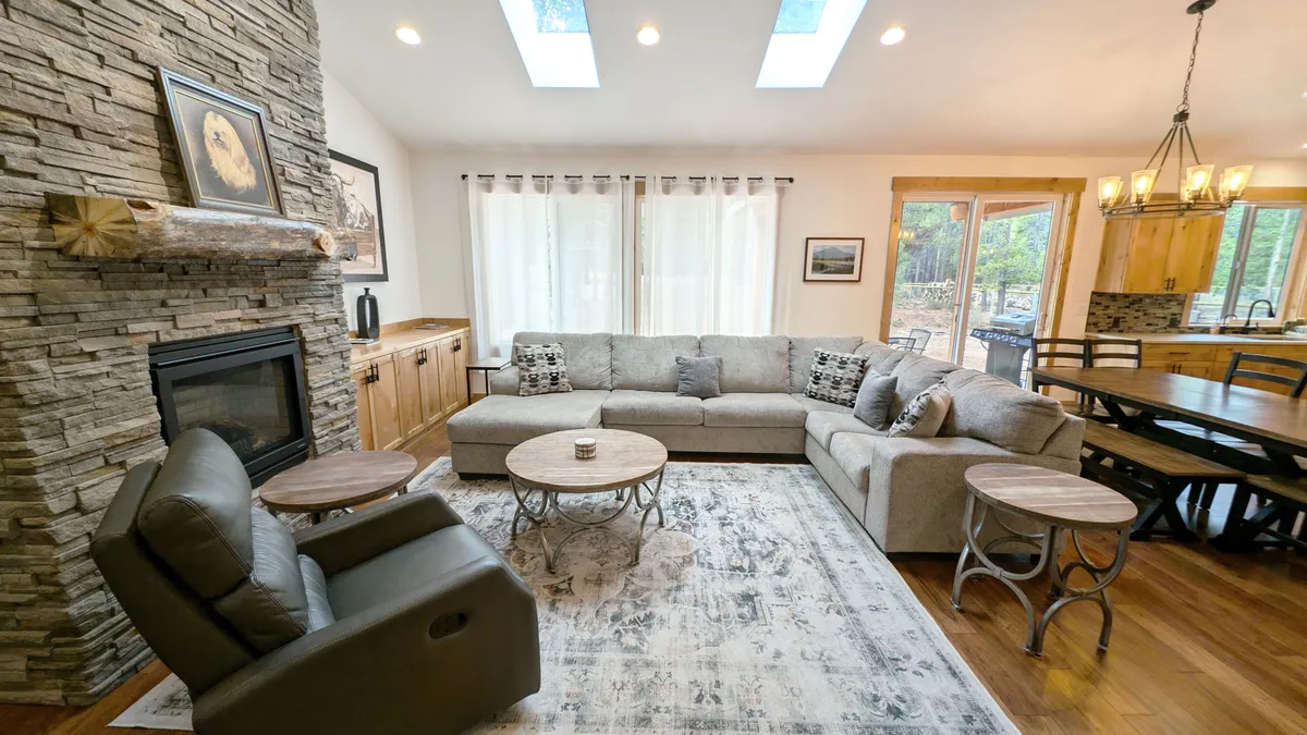 This photo focuses on the living and dining spaces from another angle, showcasing a large stone fireplace, a generous sectional sofa, and a wooden dining area. Visible wood accents and artwork on the walls enhance the warmth and welcoming mood of the space.