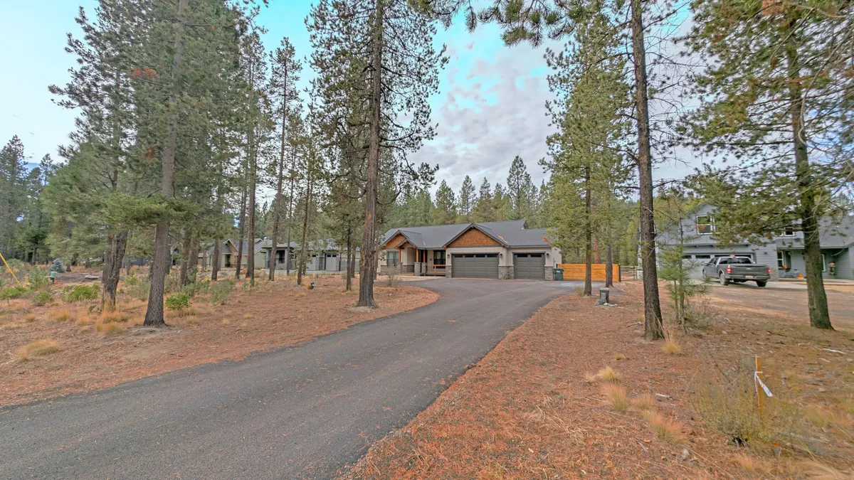 This exterior image captures the home nestled among mature trees, with a clear view of the house, the driveway, and an inviting natural setting. The tranquil mood and surrounding greenery evoke the atmosphere of Central Oregon's forests, creating a sense of privacy and a perfect home base for outdoor adventures.