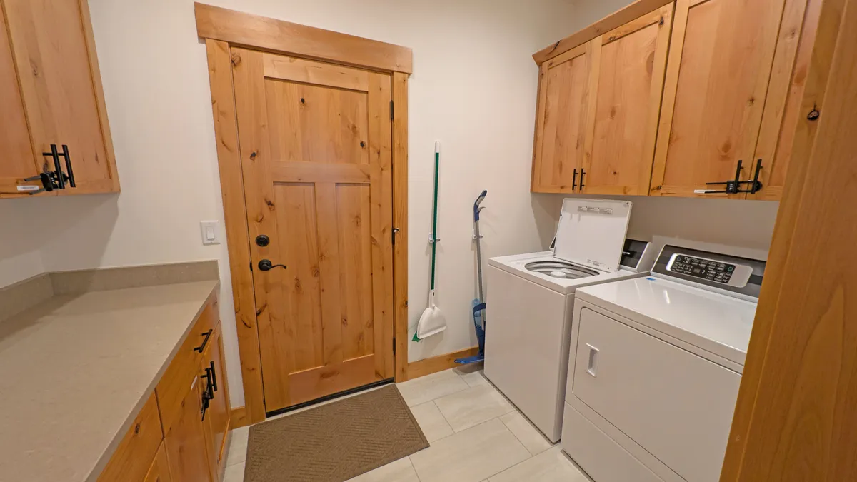 A cozy and practical laundry room featuring a commercial-grade washer and dryer, wooden cabinetry for storage, and a sturdy door leading to the outside. The space is designed for easy organization of cleaning supplies and efficient laundry routines after an adventurous day outdoors.