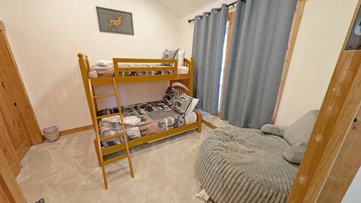 A fun, family-friendly bunk room with a pyramid bunk bed, an oversized bean bag chair, and playful curtains. Decorative art on the wall adds a whimsical touch, creating a space perfect for kids or teens to relax and play.