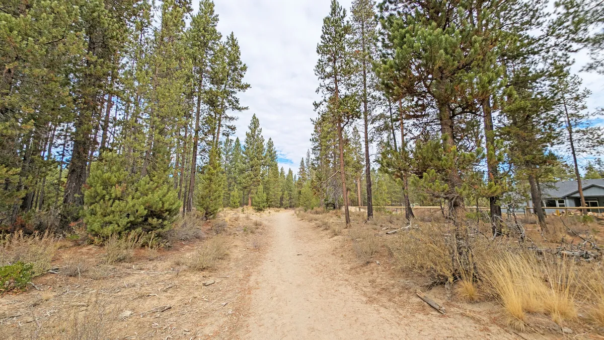 A dirt path winds through tall pine trees, leading away from the house and into the tranquil expanse of the Deschutes National Forest. The path hints at exploration opportunities, surrounded by the serenity of the forest.